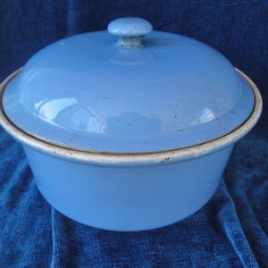 Peut inclure: Un saladier en émail bleu clair avec un couvercle assorti. Le bord du saladier est blanc et le couvercle est orné d'un petit bouton rond. L'émail présente des signes d'usure, ce qui ajoute à son charme vintage. Un article de cuisine classique.