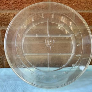 Może przedstawiać: Przezroczysta, okrągła plastikowa taca do serwowania z podzielonym wnętrzem. Taca posiada koncentryczne pierścienie i przegrody promieniowe, tworząc wiele przegródek. Taca przeznaczona jest do serwowania potraw.