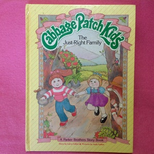 May include: A vintage Cabbage Patch Kids storybook titled "The Just-Right Family." The cover features illustrations of two Cabbage Patch Kids holding hands, set against a forest backdrop. The book is a Parker Brothers Story Book.