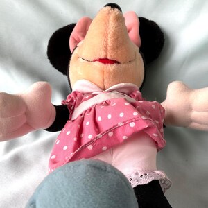 May include: A plush Minnie Mouse doll with a smiling expression. She wears a pink dress with white polka dots, a white collar, and a matching bow. Her black ears and pink bow are visible.