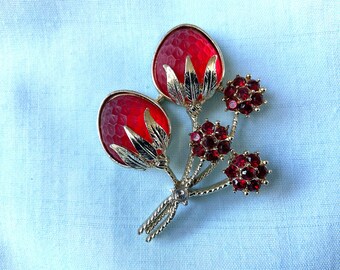 May include: A vintage floral brooch featuring two large, faceted red glass flower buds with gold-tone metal accents. The brooch also includes smaller clusters of red rhinestones and delicate gold-tone stems.