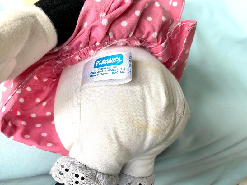 May include: A vintage Playskool plush toy, featuring a white body with a pink polka-dot dress. The tag reads "Playskool, Inc. Pawtucket, RI 02862 U.S.A. Made in Taiwan, ROC 1-6". The toy has black accents and a lace trim.