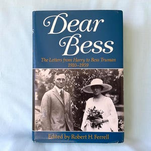 Op de afbeelding: Een hardcover boek getiteld "Dear Bess" met een donkerblauwe omslag. De titel staat in witte letters. Het boek bevat een zwart-wit foto van een man en een vrouw. De tekst "The Letters from Harry to Bess Truman 1910-1959" is ook zichtbaar.
