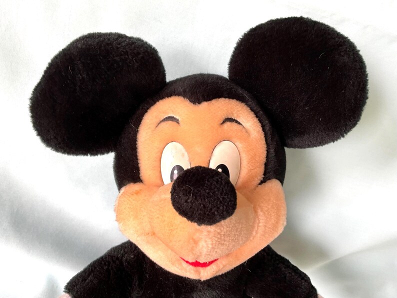 Puede incluir: Un peluche de Mickey Mouse con grandes orejas negras, una nariz negra y una cara color melocot&oacute;n. El juguete tiene una sonrisa roja y est&aacute; hecho de un material suave y difuso. Un personaje cl&aacute;sico de Disney.