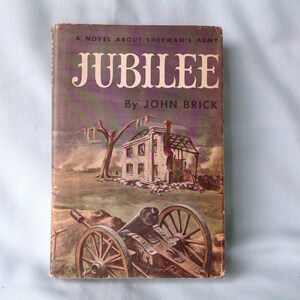 May include: Vintage book cover for "Jubilee" by John Brick. The cover art depicts a Civil War scene with a cannon in the foreground, a dilapidated house, and a barren tree under a purple sky. The title is in large, ornate letters.