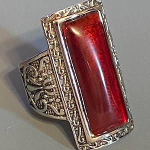 May include: A silver ring with an ornate design and a large, rectangular, red gemstone.