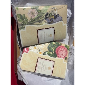 May include: Two decorative boxes with floral designs. One box features purple irises and white flowers, while the other showcases a pink rose. Both boxes have a cream-colored background with the text "Anna Griffin" and "Beautiful Bouquets".