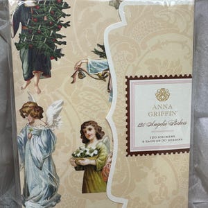 May include: A package of 120 angelic stickers by Anna Griffin. The stickers feature vintage illustrations of angels with wings, holding flowers and bells, and carrying a Christmas tree. The packaging is beige with a decorative pattern.