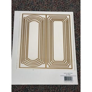 May include: A set of gold-colored slimline card compendium dies on a white background. The dies are nested in rectangular and arched shapes. The product is labeled "ANNA GRIFFIN" and "SLIMLINE CARD COMPENDIUM DIES".