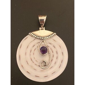 May include: A round pendant with a white and brown spiral design. The pendant has a silver-colored bail and a silver-colored decorative element with a purple gemstone in the center. The pendant is likely made of shell.