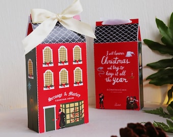May include: Two red and black Christmas gift boxes with a festive design. One box features a quote from "A Christmas Carol" and the other box features a depiction of Scrooge and Marley's counting house.