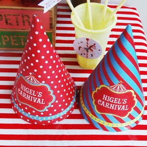 May include: Two party hats with "Nigel's Carnival" text. One hat is red with white polka dots, the other is blue and red striped. Both have a decorative label with a circus tent design. A yellow cup with straws and a small flag are also visible.