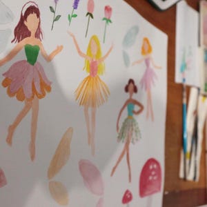 May include: Watercolor illustrations of fairies in various poses, with flower accents. The fairies are depicted with colorful dresses and hairstyles. The artwork is on white paper, with a wooden surface in the background.