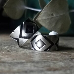 May include: Two silver ear cuffs with a geometric design. The cuffs are made of metal and have a brushed finish.