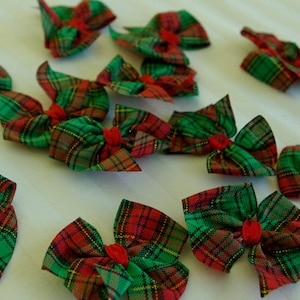 May include: Twelve red and green tartan bows with a red centre. The bows are made of fabric and are perfect for decorating for the holidays.