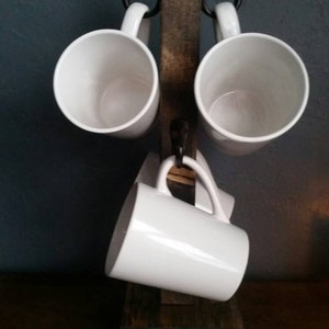 Pu&ograve; includere: Un porta tazze in legno rustico con quattro tazze in ceramica bianca appese a ganci in metallo nero. Il supporto &egrave; realizzato in legno riciclato e ha una finitura naturale.