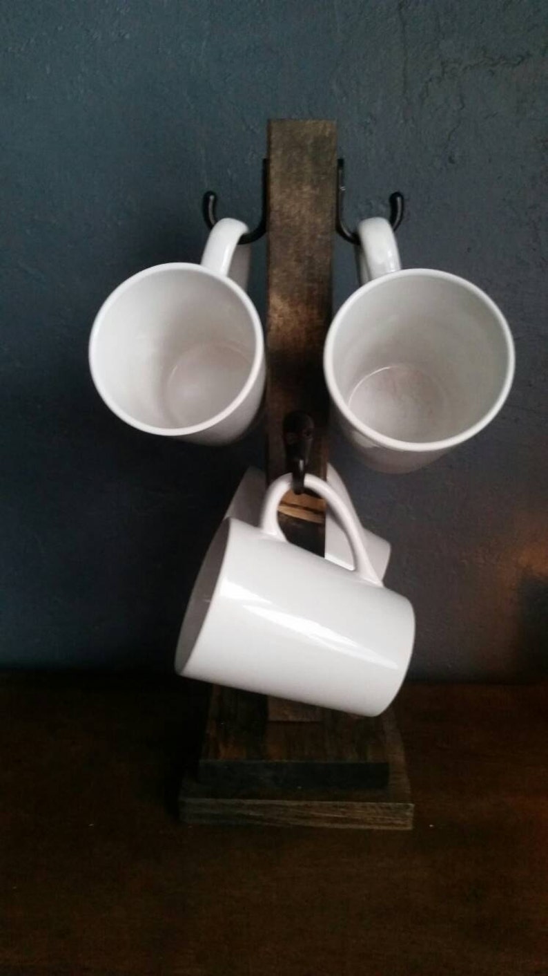 Pu&ograve; includere: Un porta tazze in legno rustico con quattro tazze in ceramica bianca appese a ganci in metallo nero. Il supporto &egrave; realizzato in legno riciclato e ha una finitura naturale.