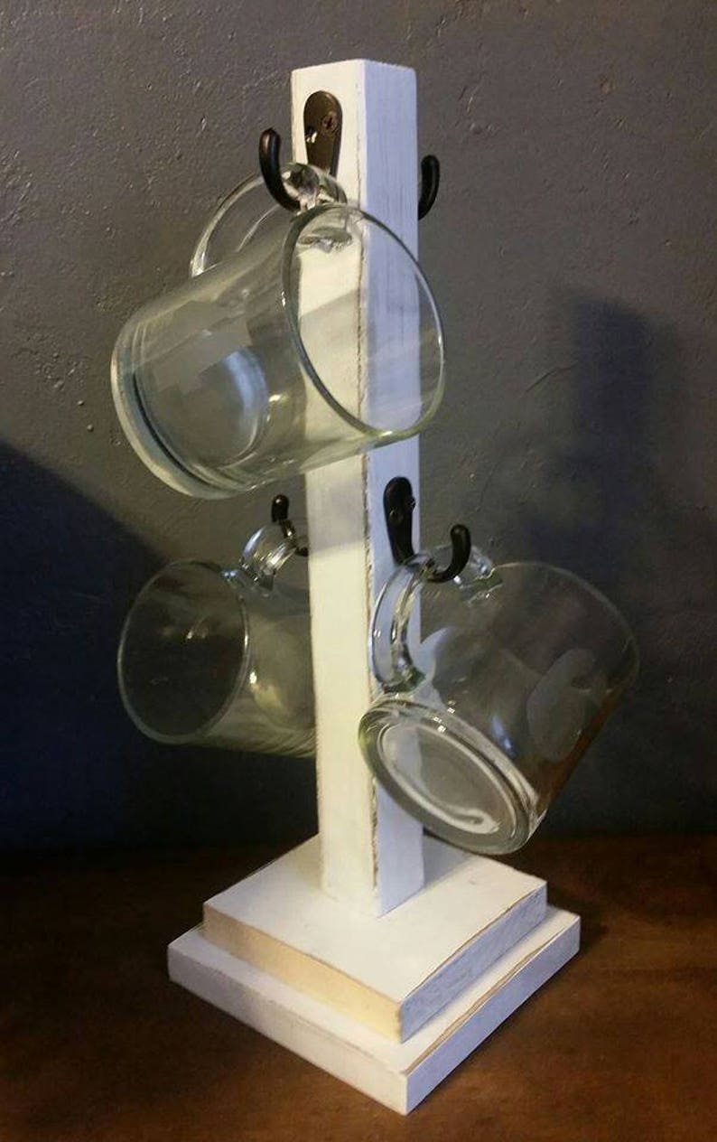 Pu&ograve; includere: Un porta tazze in legno bianco con quattro ganci e una base a pi&ugrave; livelli. Il porta tazze contiene quattro tazze di vetro trasparente.