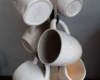 May include: A wooden mug rack with six white ceramic mugs hanging from hooks. The mugs have the words "BAE" and "BE YOU" written on them. The rack is made of rustic wood and has a natural finish.