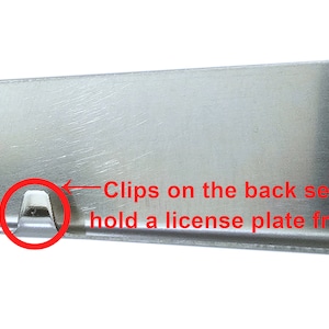 May include: Close-up of a silver license plate frame with clips on the back that securely hold a license plate frame.
