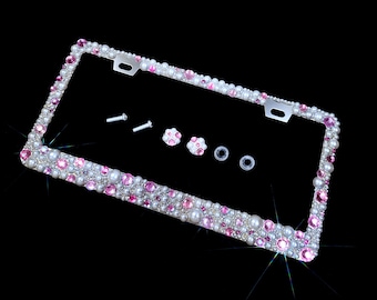 May include: A silver license plate frame with a border of pink and white rhinestones. The frame includes two screws and two small decorative flower-shaped rhinestones.