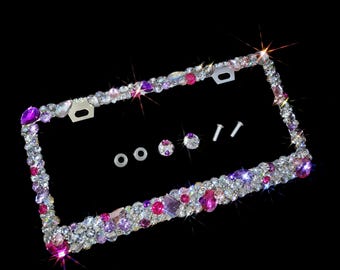 May include: A silver license plate frame with clear and pink rhinestones. The frame is decorated with a variety of sizes and shapes of rhinestones.