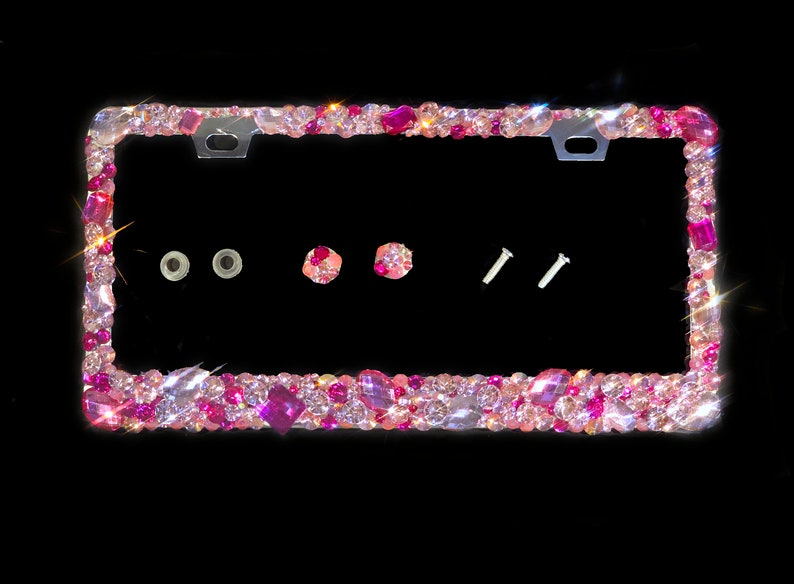 May include: A pink and clear crystal embellished license plate frame. The frame has two screw holes and two small plastic caps.