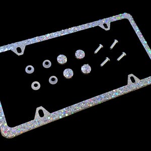 May include: A silver glitter license plate frame with crystal embellishments and mounting hardware. The frame is rectangular with rounded corners and an iridescent finish. Includes screws and washers.