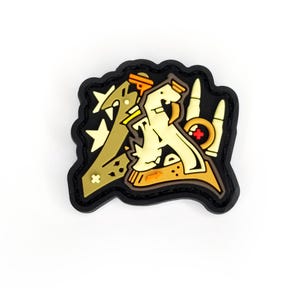 Może przedstawiać: Czarno-żółta naszywka haftowana ze stylizowanym wzorem pistoletu i innych przedmiotów. Naszywka ma kształt litery A.