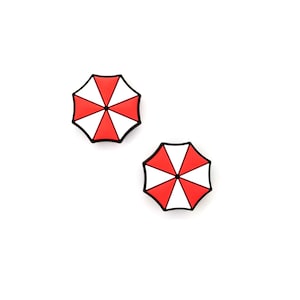May include: Two small, umbrella-shaped accessories with a red and white segmented design and a black outline. The accessories are set against a white background.