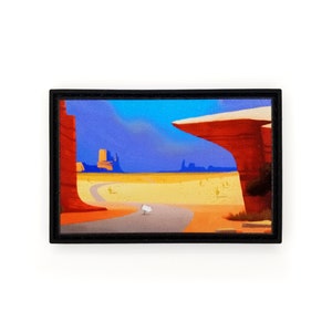 May include: A framed illustration depicting a desert landscape with a winding road leading to a large rock formation. The sky is blue with white clouds and the ground is a sandy yellow.