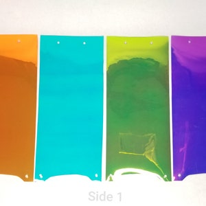 Può includere: Quattro fogli rettangolari di vinile iridescente in arancione, turchese, verde e viola. I fogli sono appesi su uno sfondo bianco. Il testo "Side 1" è stampato sotto i fogli.