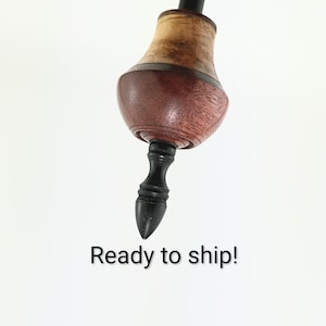 Puede incluir: Una peonza de madera hecha a mano con un cuerpo bulboso y multicolor. La parte superior presenta una sección superior de madera de color claro, una sección media marrón rojizo oscuro y una base negra. El texto "Ready to ship!" está en la parte inferior.