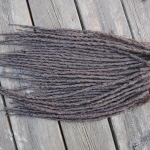 Könnte beinhalten: Ein Bündel dunkelbrauner synthetischer Dreadlocks, in Reihen angeordnet, auf einer Holzoberfläche.