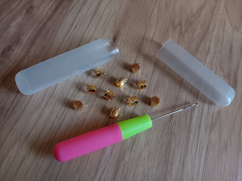 Może przedstawiać: Zestaw złotych metalowych koralik&oacute;w, r&oacute;żowo-zielony szydełko i dwa przezroczyste plastikowe pojemniki do przechowywania.