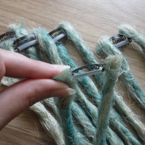 May include: A set of teal and white synthetic dreadlocks with metal clips attached to the ends.