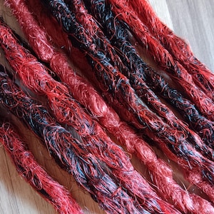 Peut inclure: Gros plan sur plusieurs dreadlocks aux tons rouges et noirs. Les mèches de cheveux synthétiques sont étroitement torsadées, créant un aspect texturé. La combinaison de couleurs offre un contraste visuel audacieux et saisissant, adapté aux coiffures alternatives.