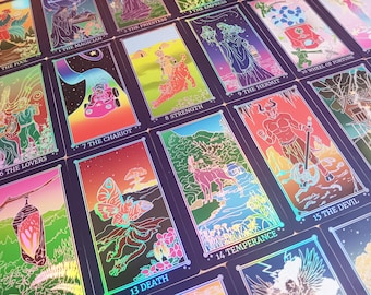 May include: A collection of tarot cards with vibrant illustrations and holographic accents. Each card features unique artwork and titles such as "The Lovers," "The Chariot," and "The Devil." The cards are arranged in a visually appealing display.