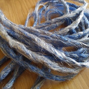 May include: A bundle of synthetic dreadlocks in shades of blue and gray. The dreadlocks are long and thick, and they are arranged in a loose pile.