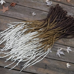 May include: A set of synthetic dreadlocks with a two-tone ombre colour scheme. The dreadlocks are white at the bottom and transition to a brown colour at the top.