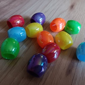 May include: A collection of colorful, oval-shaped plastic beads with a glossy finish. The beads are arranged in a rainbow pattern.