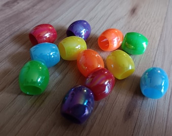 May include: A collection of colorful, oval-shaped plastic beads with a glossy finish. The beads are arranged in a rainbow pattern.