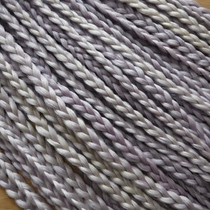 May include: A close-up of a bundle of braided hair extensions in a light purple and white color.