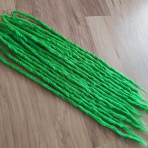 Könnte beinhalten: Ein Bündel leuchtend grüner synthetischer Dreadlocks. Die Dreadlocks sind lang und dick und zu einem ordentlichen Stapel angeordnet.