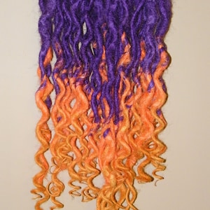 May include: Purple and orange ombre synthetic dreadlocks hanging from a black rod. The dreadlocks are curly and have a textured appearance.