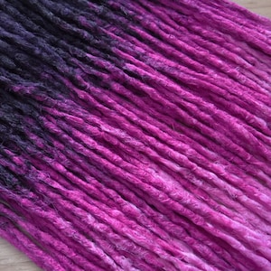 Könnte beinhalten: Ein Satz synthetischer Dreadlocks mit einem Farbverlauf von Schwarz zu Pink. Die Dreadlocks bestehen aus Kanekalon-Haar und sind etwa 61 cm lang.
