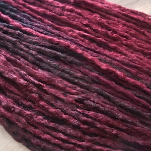 Könnte beinhalten: Ein Set langer, synthetischer Dreadlocks in einem dunklen Burgunder- und Schwarz-Ombre-Farbton. Die Dreadlocks sind aus Kanekalon-Haar gefertigt und bereit zum Einsetzen.