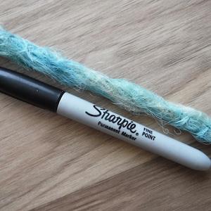 Könnte beinhalten: Nahaufnahme einer blauen und weißen synthetischen Dreadlock mit einem schwarzen Sharpie Permanentmarker mit feiner Spitze daneben.