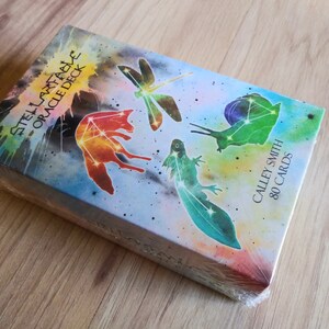 May include: A box of Stella Maris Oracle Deck cards with a watercolor background and images of a fox, dragonfly, snail, and newt. The box is labeled "Stella Maris Oracle Deck" and "Calley Smith 80 Cards".
