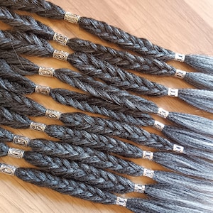 May include: Multiple black and grey braided hair extensions with silver beads. The hair extensions are ombre, transitioning from black to grey.